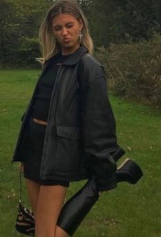 a woman is standing in the grass with her hand on her hip and wearing black boots