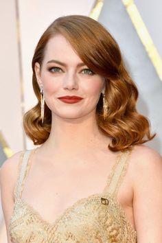 a woman with long red hair wearing a gold dress and large earrings on her head