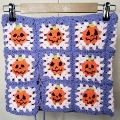 a crocheted blanket with pumpkins and daisies in the center, hanging on a hook