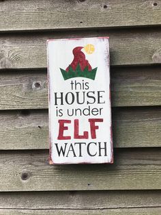 this house is under elf watch sign hanging on the side of a wooden building with wood siding