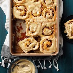 a pan filled with cinnamon rolls covered in icing next to a bowl of sauce