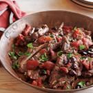 a bowl filled with meat and vegetables on top of a wooden table next to plates