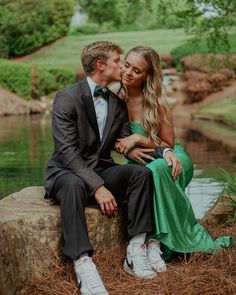 a man and woman sitting next to each other in front of a pond with trees