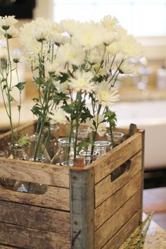 white flowers are arranged in glass vases in a wooden crate on a table top