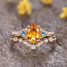 an orange and blue diamond ring sitting on top of a piece of wood with flowers in the background