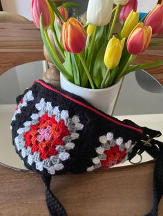 a crocheted purse sitting on top of a table next to a vase filled with tulips