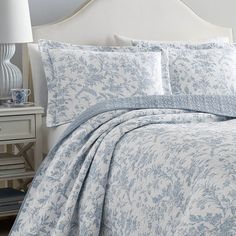 a bed with blue and white comforters in a bedroom next to a night stand