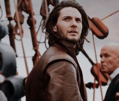 a man with long hair standing next to another man on a boat in the ocean