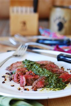 a white plate topped with meat covered in pesto next to a fork and knife