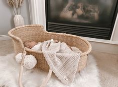 a baby is laying in a basket next to a fireplace with a blanket on it