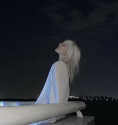 a woman with white hair is standing on a ledge looking up at the night sky