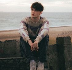 a young man sitting on top of a stone wall next to the ocean