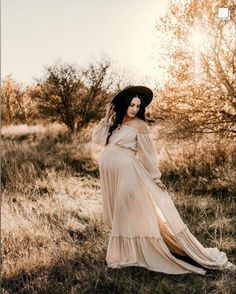 a pregnant woman in a long dress and hat poses for the camera while wearing a black hat