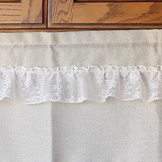 a close up of a white curtain on a wooden window sill with lace trim