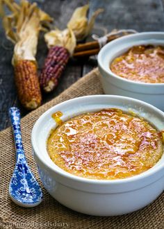 two white bowls filled with soup next to corn on the cob and a blue spoon