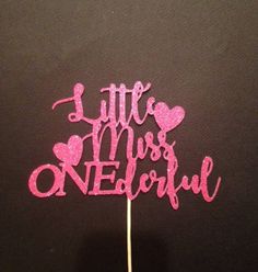 a little miss onederful cake topper on a black table with pink glitter