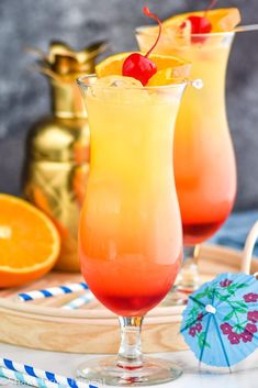 two glasses filled with orange juice and topped with a cherries on the rim, next to an orange slice