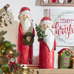 two red santa clause figurines sitting on top of a mantle next to a christmas tree