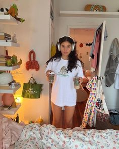 a young woman is standing in her bedroom with clothes on the rack and holding a cup