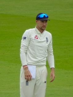 a man standing on top of a green field wearing a white shirt and blue hat