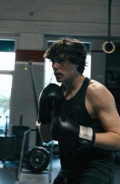 a man wearing black boxing gloves in a gym area with his hands behind his back