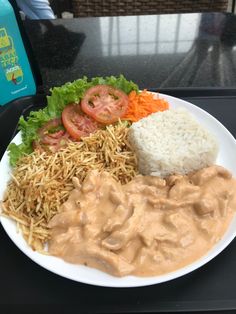 a white plate topped with rice and veggies next to a bowl of sauce