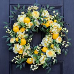 a wreath with lemons and white flowers on a black front door, surrounded by greenery