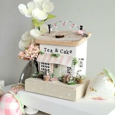 a tea and cake stand with flowers on the table next to it, in front of a white wall