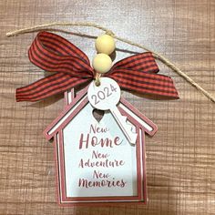 a new home ornament hanging on a wooden table with a red and white ribbon