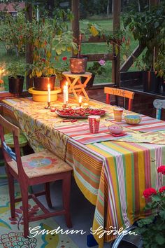 a table set for two with candles on it and flowers in the back ground, surrounded by potted plants