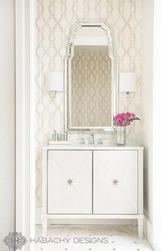 a white vanity with a mirror and flowers on it in a room that has wallpaper