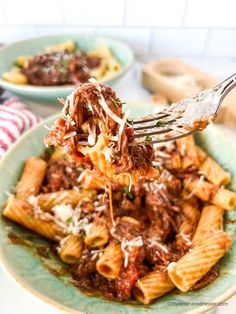 a fork full of pasta with meat sauce and parmesan cheese on the side