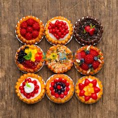 nine pies are arranged in the shape of fruit tarts on a wooden table