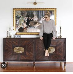 a woman sitting on top of a cabinet in front of a painting