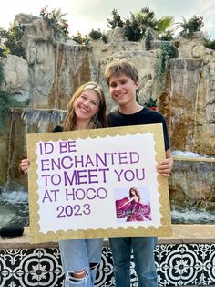 two people holding up a sign that says i'd be enchanted to meet you at hogo