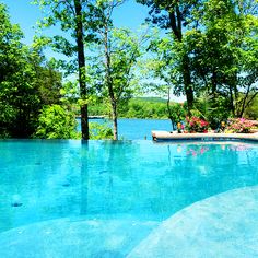 an empty swimming pool surrounded by lush green trees and blue water with flowers on the edge