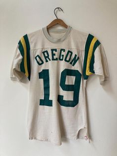 True vintage 1960's athletic Jersey. All cotton jersey with crunchy lettering, and a couple holes as per pictures. Total winner, this one is. Tag: Hanesport- Men's S 34/36 Fabric: 100% cotton Front: OREGON 19 Back: 19 PTP: 16 3/4", Length: 26 1/2", Sleeve: 11 1/2" No refunds, returns or exchanges. You have options in shipping. We will only ship outside of North America with tracking. Varsity Cotton Jersey With Team Name, Cotton Jersey With Letter Print For Game Day, Cotton Letter Print Jersey For Game Day, Cotton Fan Gear Jersey With Short Sleeves, Cotton Short Sleeve Fan Gear Jersey, Throwback Team-colored Cotton Jersey, Sporty Cotton Jersey With Team Name, Team Spirit Cotton Jersey With Letter Print, Throwback Cotton Jersey For Sports Events