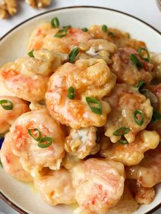 a white plate topped with shrimp and sauce covered in green garnish next to some cashews