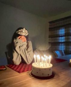 a woman sitting at a table in front of a cake with lit candles on it