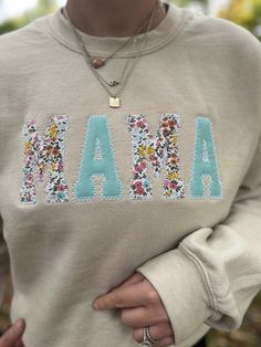 a woman wearing a sweatshirt with the word maa on it and flowers in front of her chest