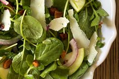 a salad with spinach, apples and cheese in a white bowl on a wooden table