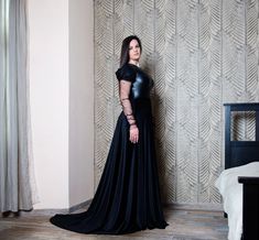 a woman in a black dress standing next to a bed