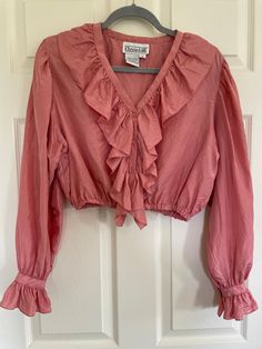 Vintage 90s 100% silk pink blouse by Christie & Jill.  Cropped fit, button front, ruffles at neck, down the front, and at wrists.  Waist elastic is very stretchy.  Has a few small marks on left shoulder and near cuff, see last 2 pictures. Pinhole near back hem and another near right side hem, does not like they will get any bigger.  See video for close up. Vintage size M.  Best for modern size M.  Be sure to check measurements and compare to a similar garment in your closet. Length 17" Shoulders 16.75" PTP 20.75" (41.5 chest) Waist 11.75" unstretched (23.5) Sleeve length 24" At this time standard shipping is a flat fee to the United States only.  Additional items ship for only one dollar.  To place an order to outside the US, please send me a message and I will reserve a listing for you wi Fitted Cropped Ruffle Blouse, Feminine Pink Cropped Blouse, Pink Stretch Blouse With Ruffles, Stretch Pink Blouse With Ruffles, Pink Feminine Crop Top With Ruffles, Pink Ruffled Crop Top For Spring, Stretch Ruffled Long Sleeve Crop Top, Stretch Long Sleeve Crop Top With Ruffles, Pink Fitted Top With Ruffled Collar