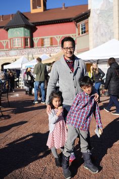 a man standing next to two small children in front of a building with people around it