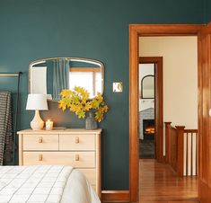 a bedroom with green walls and wooden floors, white bedding and dressers in the foreground