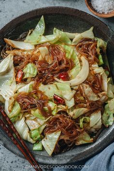 a bowl filled with noodles and vegetables on top of a table next to chopsticks