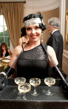 a woman in a black dress holding two wine glasses