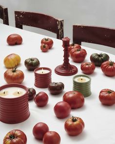 tomatoes and candles are arranged on a white tablecloth with red, green, and yellow candle holders