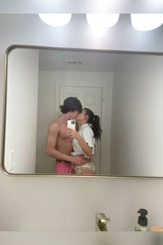 a man and woman kissing in front of a mirror