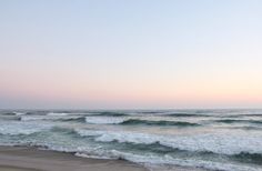 the ocean waves are rolling in and out of the water at sunset or dawn on an empty beach